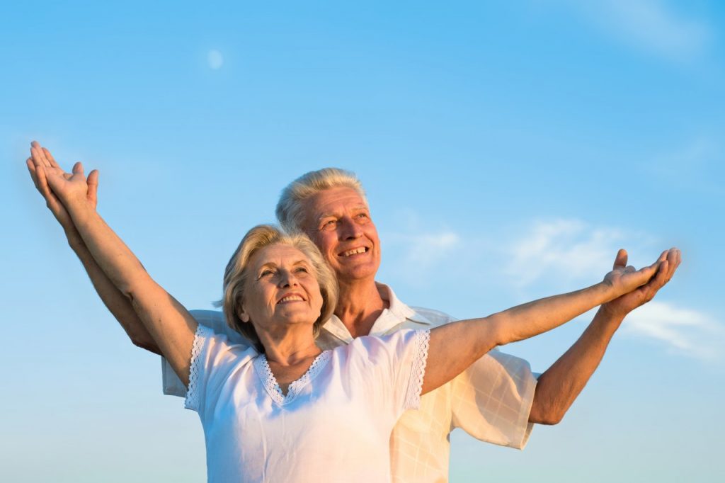 Um casal de idosos abraçados olhando para o céu azul