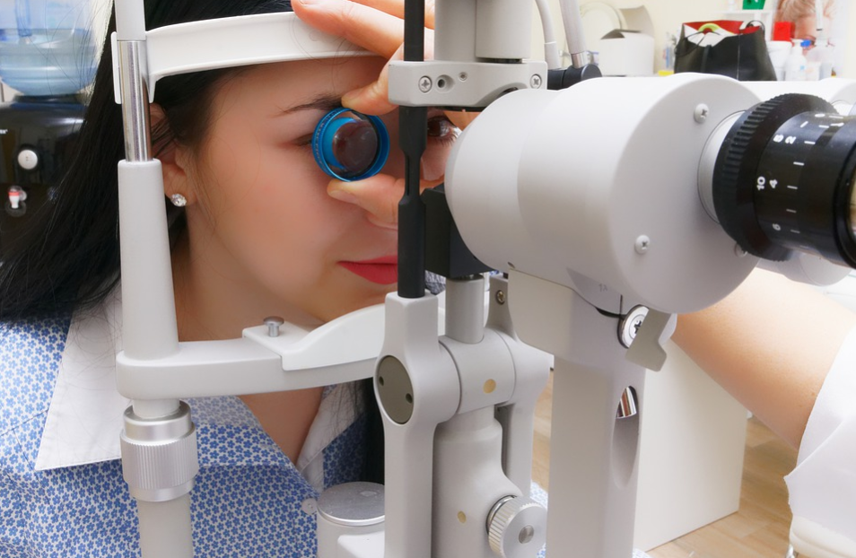 mulher asiática usando camisa azul se prepara para realizar exame oftalmológico em máquina de cor branca