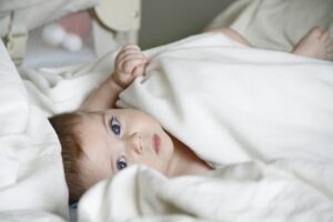 Imagem de um bebê deitado na cama enrolado em um lençol branco