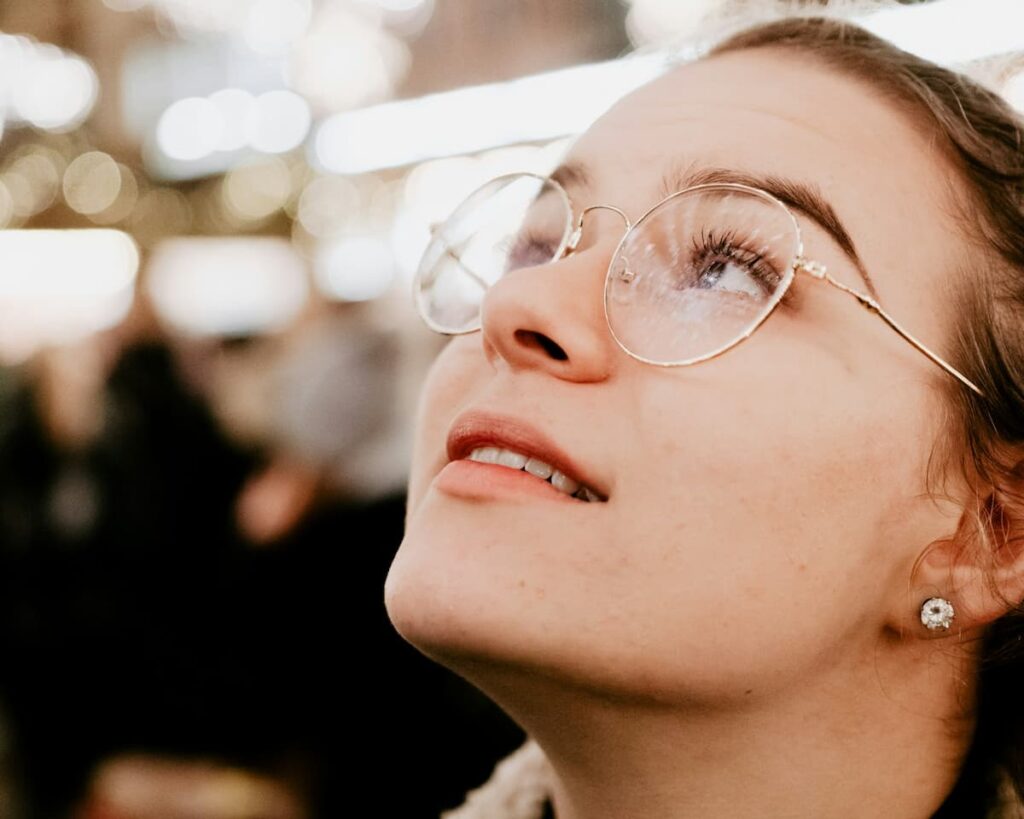 Imagem de uma mulher de óculos olhando para cima em um ambiente com luzes