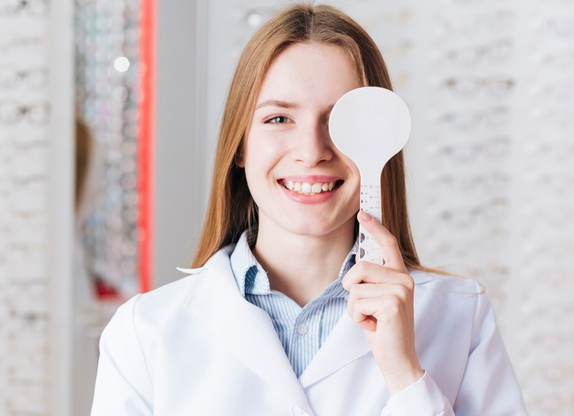 médica usando avental branco mostrando instrumento em frente ao seu olho esquerdo