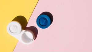 em uma mesa laranja e rosa encontra-se um pote de lente de contato ao lado de uma de suas tampas de cor azul