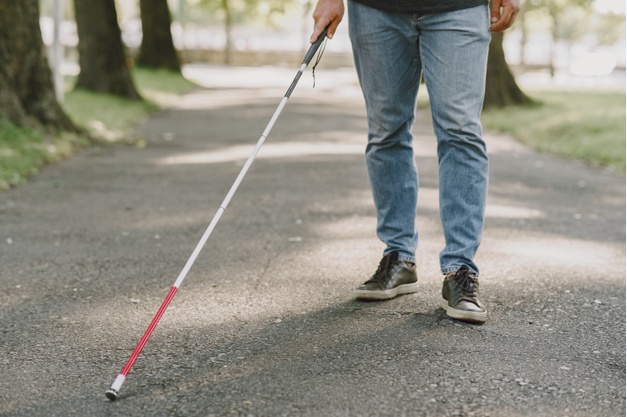 imagem das pernas e bengala de uma pessoa com deficiência visual caminhando no parque