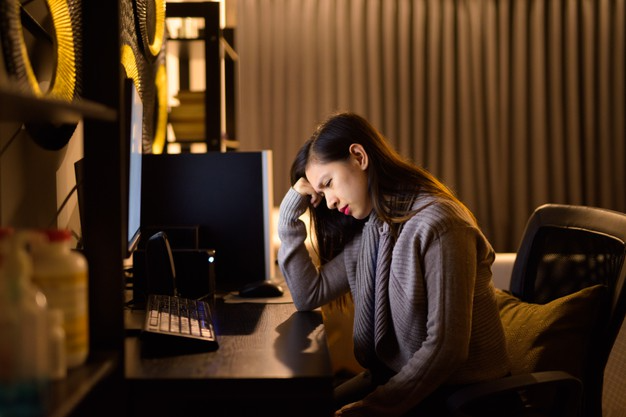 mulher com vista cansada em frente a um computador apoiando sua cabeça sobre sua mão