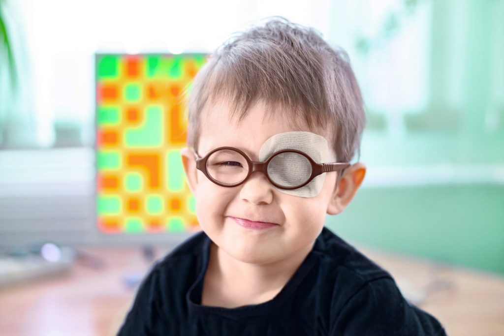Criança usando óculos e tapa olho.