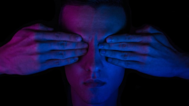 Homem cobre os olhos com as mãos devido a protanopia