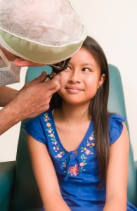 menina sentada no oftalmologista, que realiza exame ocular nela, tal como a ultrassonografia ocular