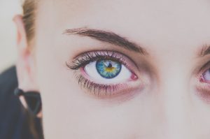 Imagem focada em olho verde de uma mulher, que está olhando diretamente para a câmera