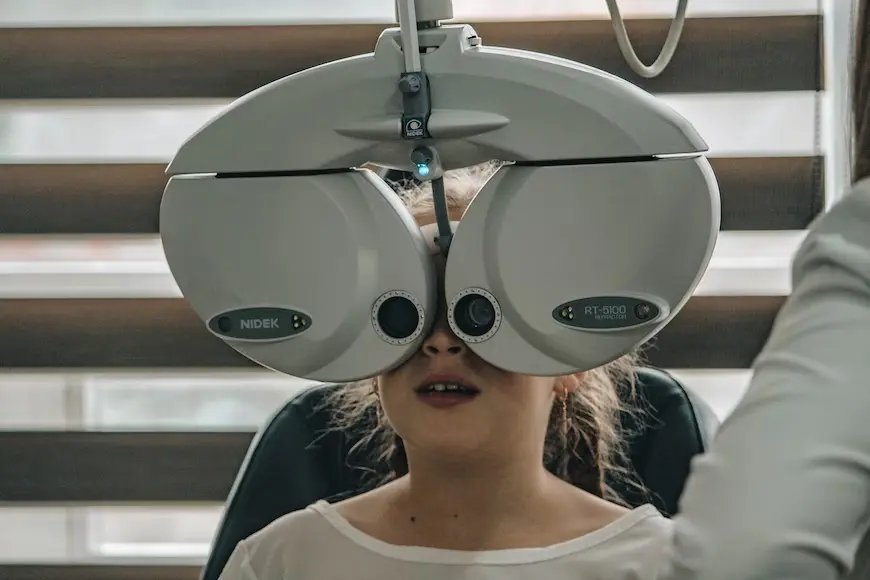 criança sentada na cadeira de oftalmologista com aparelho de teste ocular no rosto