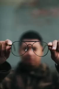 Homem ao fundo embaçado segurando óculos de grau a frente da lente
