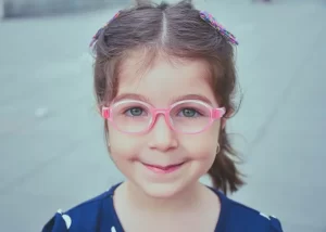 Rosto de menina sorrindo de boca fechada usando óculos de grau cor de rosa