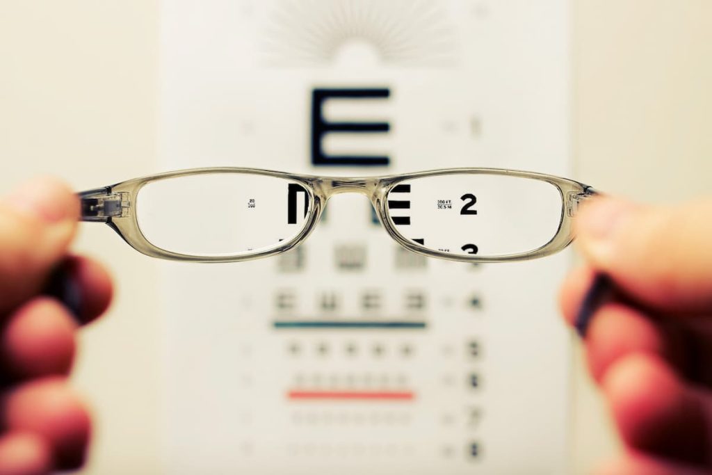 Umapessoa segurando um óculos com grau na frente de umas letras