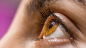 A imagem apresenta uma fotografia em macro e em perfil (visão diagonal/lateral) de um olho humano aberto, focando nos detalhes da íris e dos cílios.