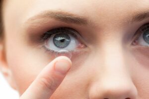 Mulher de olhos claros com lente intraocular na mão colocando nos olhos.