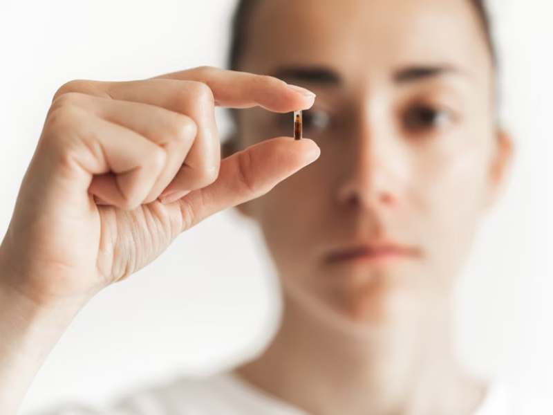 A imagem mostra uma pessoa segurando uma pequena cápsula com atenção e seriedade. Isso transmite a importância dos suplementos concentrados no cuidado com a saúde — especialmente a ocular.
