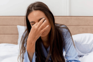 A imagem mostra uma mulher deitada, com a mão sobre os olhos, em aparente desconforto ocular ou dor de cabeça.