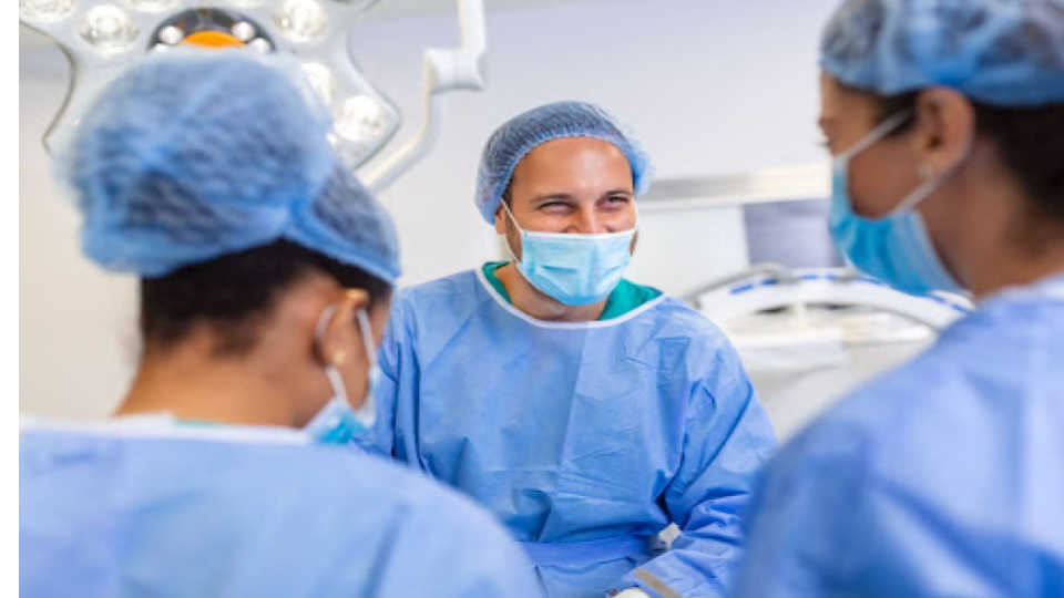 A imagem mostra uma equipe médica em um ambiente hospitalar, provavelmente em uma sala cirúrgica.