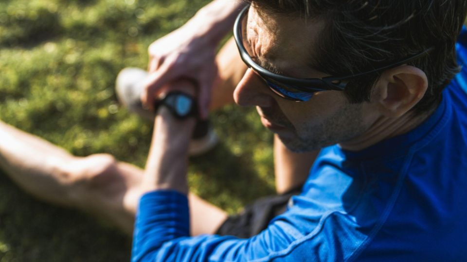 A imagem mostra um homem praticando atividade física ao ar livre, sentado sobre a grama em um ambiente iluminado pela luz natural do sol.