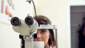 A imagem mostra uma paciente realizando um exame oftálmico em um consultório médico.